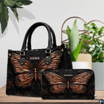 Copper butterfly handbag and matching wallet displayed together on a wooden tabletop near houseplants.