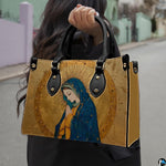 Model holding gilded Renaissance Virgin Mary handbag outdoors on street.