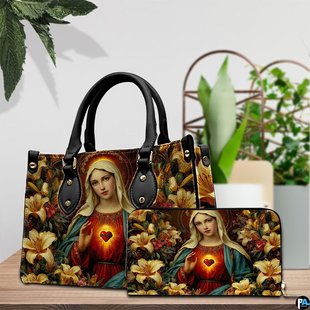 Our Lady of Lilies handbag and wallet set displayed together on table beside green plants