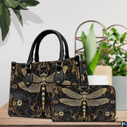 Tabletop lifestyle presentation of gold dragonfly handbag and matching wallet with potted plants