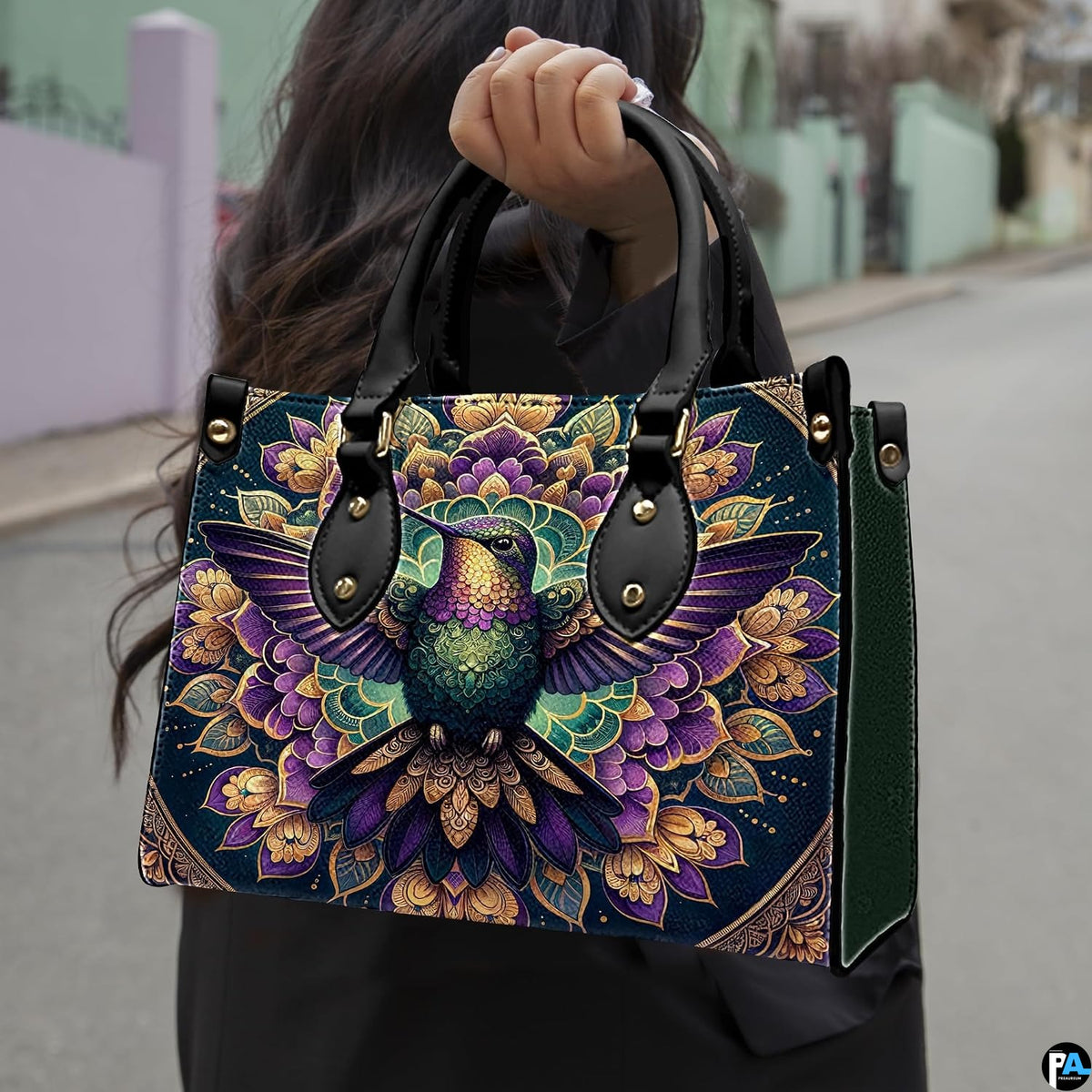 Model holding mandala hummingbird handbag outdoors displaying rich ornamental avian artwork.