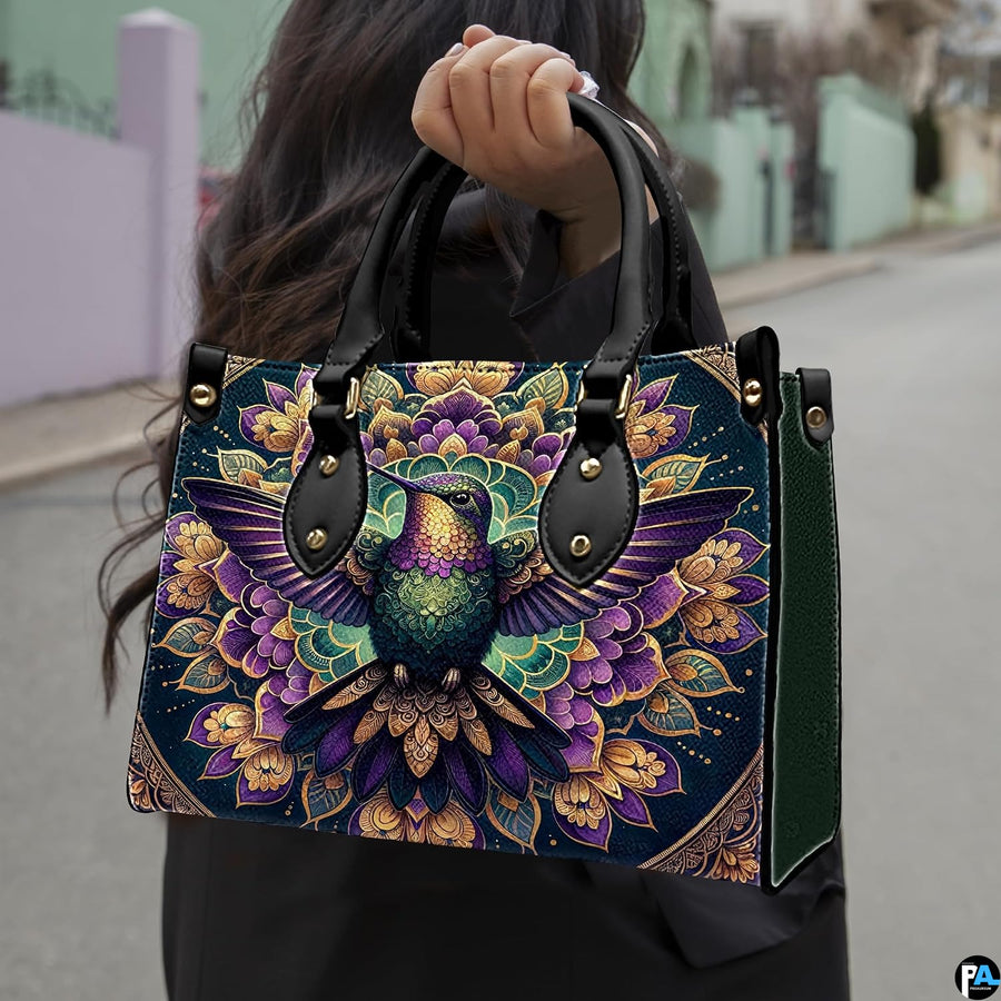 Model holding mandala hummingbird handbag outdoors displaying rich ornamental avian artwork.