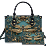 Studio display of embossed gold dragonfly handbag and matching wallet with botanical wreath on teal