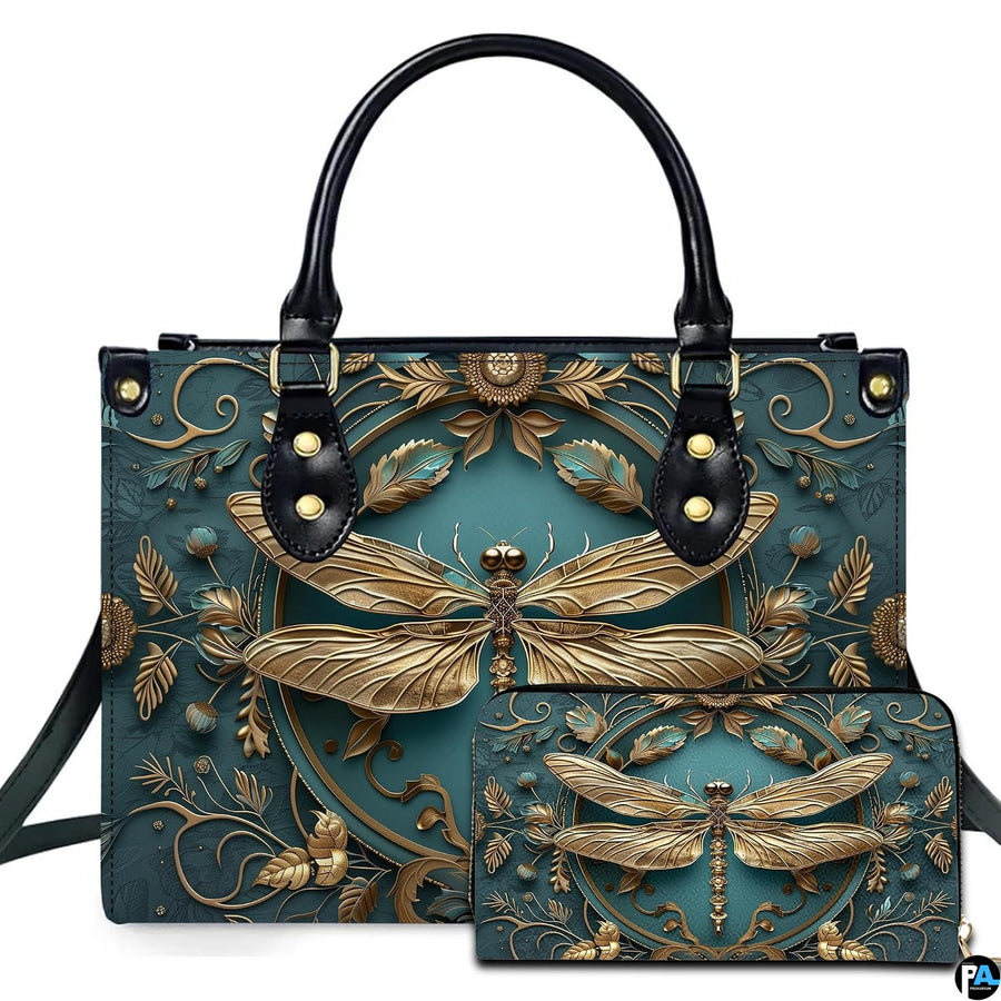Studio display of embossed gold dragonfly handbag and matching wallet with botanical wreath on teal