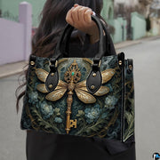 Three-quarter view of dragonfly key purse showing structured shape, handles, and gold accents