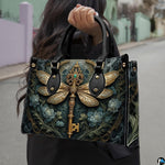 Three-quarter view of dragonfly key purse showing structured shape, handles, and gold accents