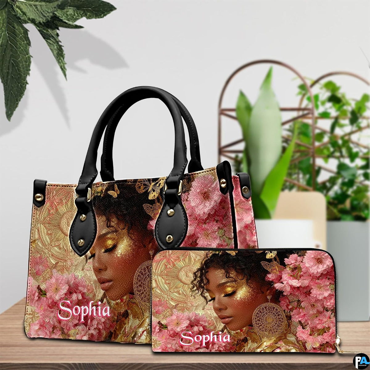 Tabletop styling showing golden glow afro art piece and companion wallet beside green foliage.