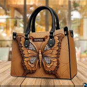 Sculpted tan butterfly handbag resting on a sunny outdoor wooden deck in front of large glass windows.