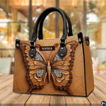 Sculpted tan butterfly handbag resting on a sunny outdoor wooden deck in front of large glass windows.