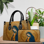 Handbag and matching wallet with gilded Virgin Mary artwork displayed beside indoor plant.