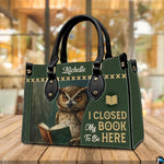 Three-quarter perspective view of green reading owl handbag resting on a rustic wooden table.