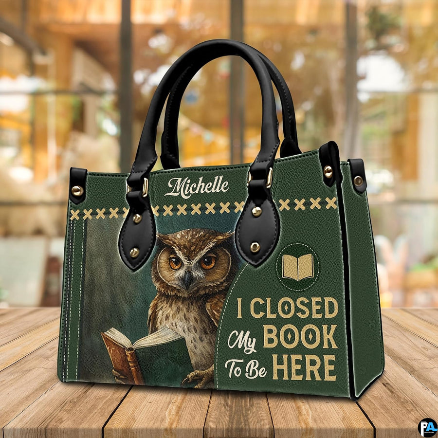 Three-quarter perspective view of green reading owl handbag resting on a rustic wooden table.