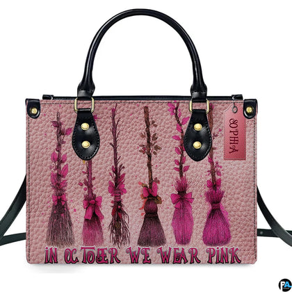 Witch broom art accessory displaying rustic sweepers decorated in pink ribbons against blush paneling.