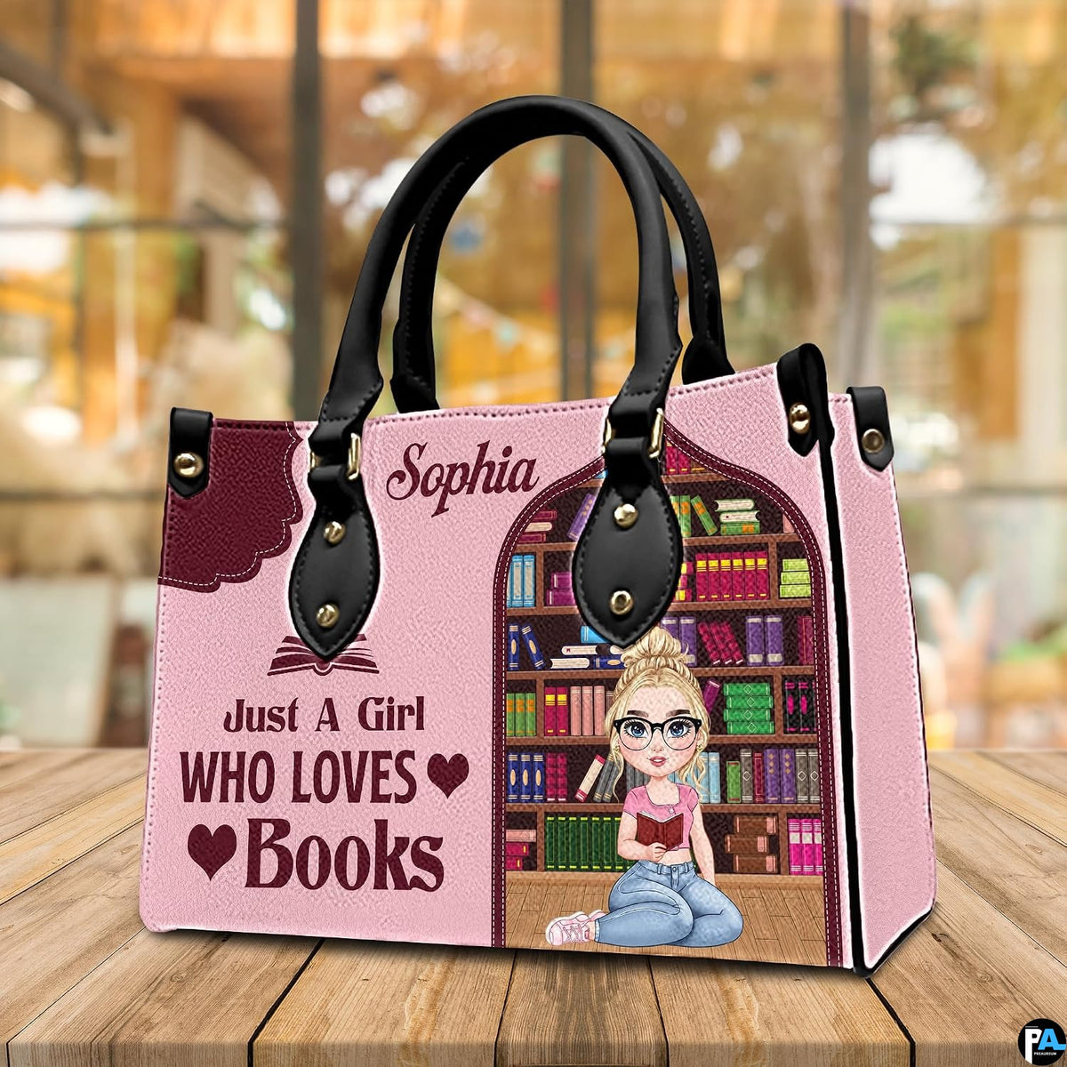 Three-quarter perspective view of pink reading girl handbag on a rustic wooden table.