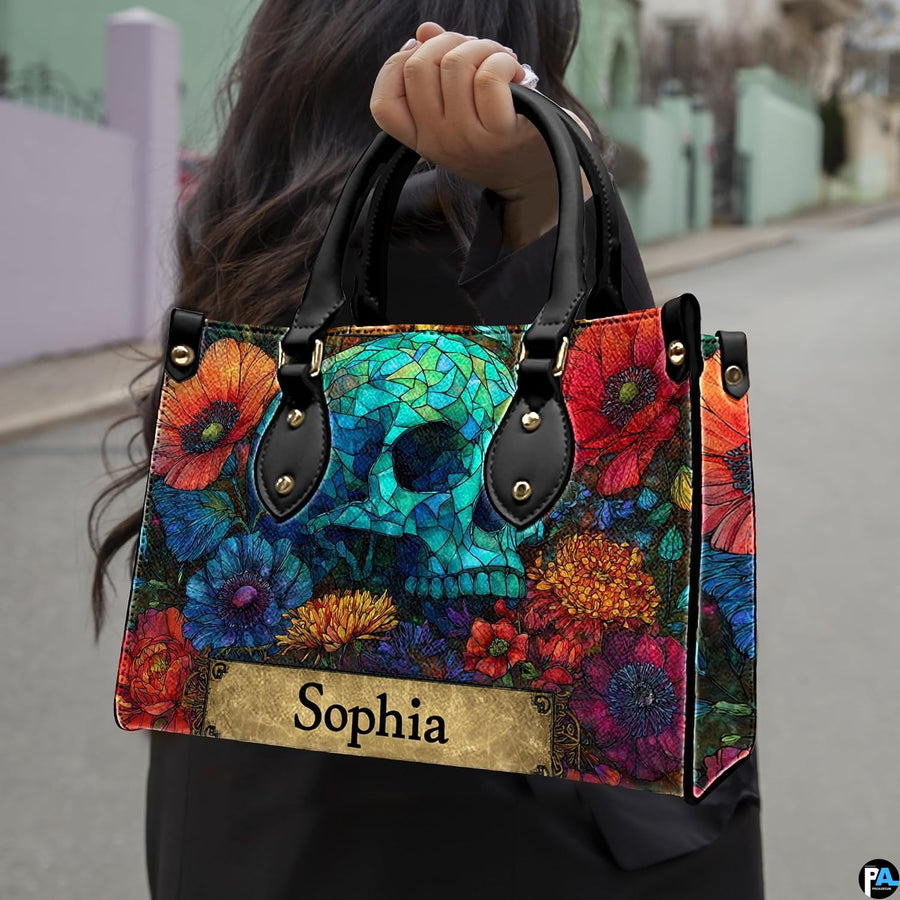 Stained glass skull handbag carried outdoors by top handle along residential street.