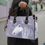 Side profile of crowned unicorn handbag showing structured silhouette and black carrying handles.
