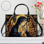 Devotional stained glass handbag staged indoors beside a decorative flower vase