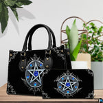 Gothic pentagram handbag and wallet on wooden table beside houseplant.