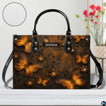 Bronze butterfly handbag displayed on a white surface alongside floral decor and a circular material swatch.