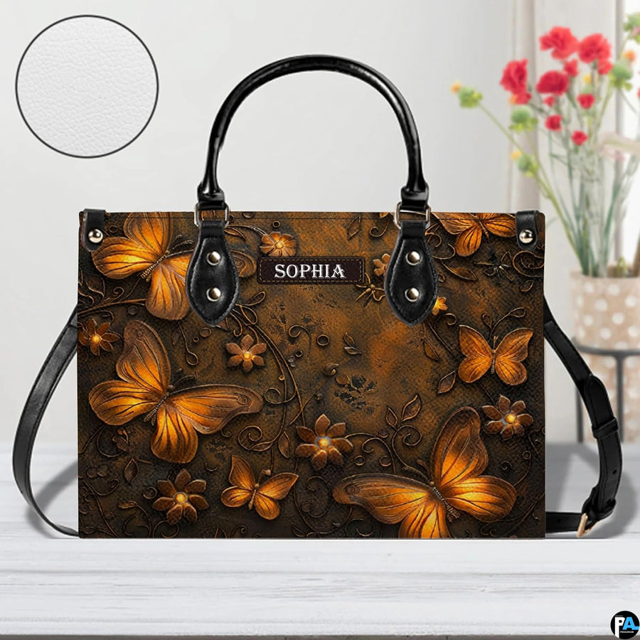 Bronze butterfly handbag displayed on a white surface alongside floral decor and a circular material swatch.