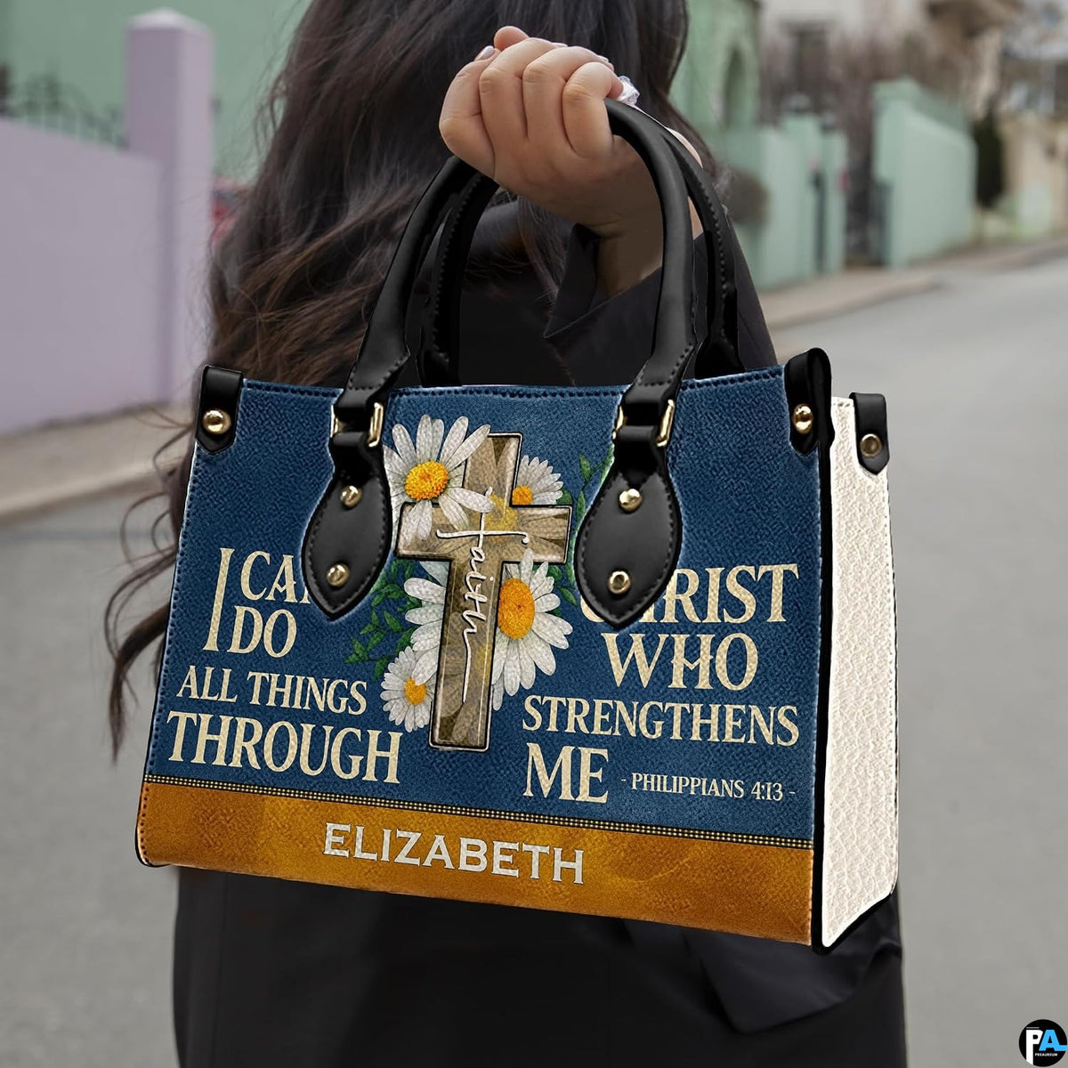 Navy handbag carried outdoors by top handles displaying the wooden cross and daisy artwork.