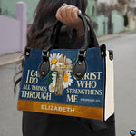 Navy handbag carried outdoors by top handles displaying the wooden cross and daisy artwork.