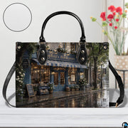 Angled view displaying the reflective wet cobblestone street and shop facade across the structured handbag.