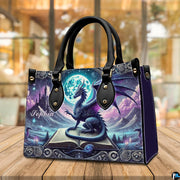Dragon art handbag resting on wooden tabletop under warm ambient cafe lighting.