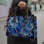 Front view of sapphire butterfly handbag showcasing glowing blue wings and pale flower petals.