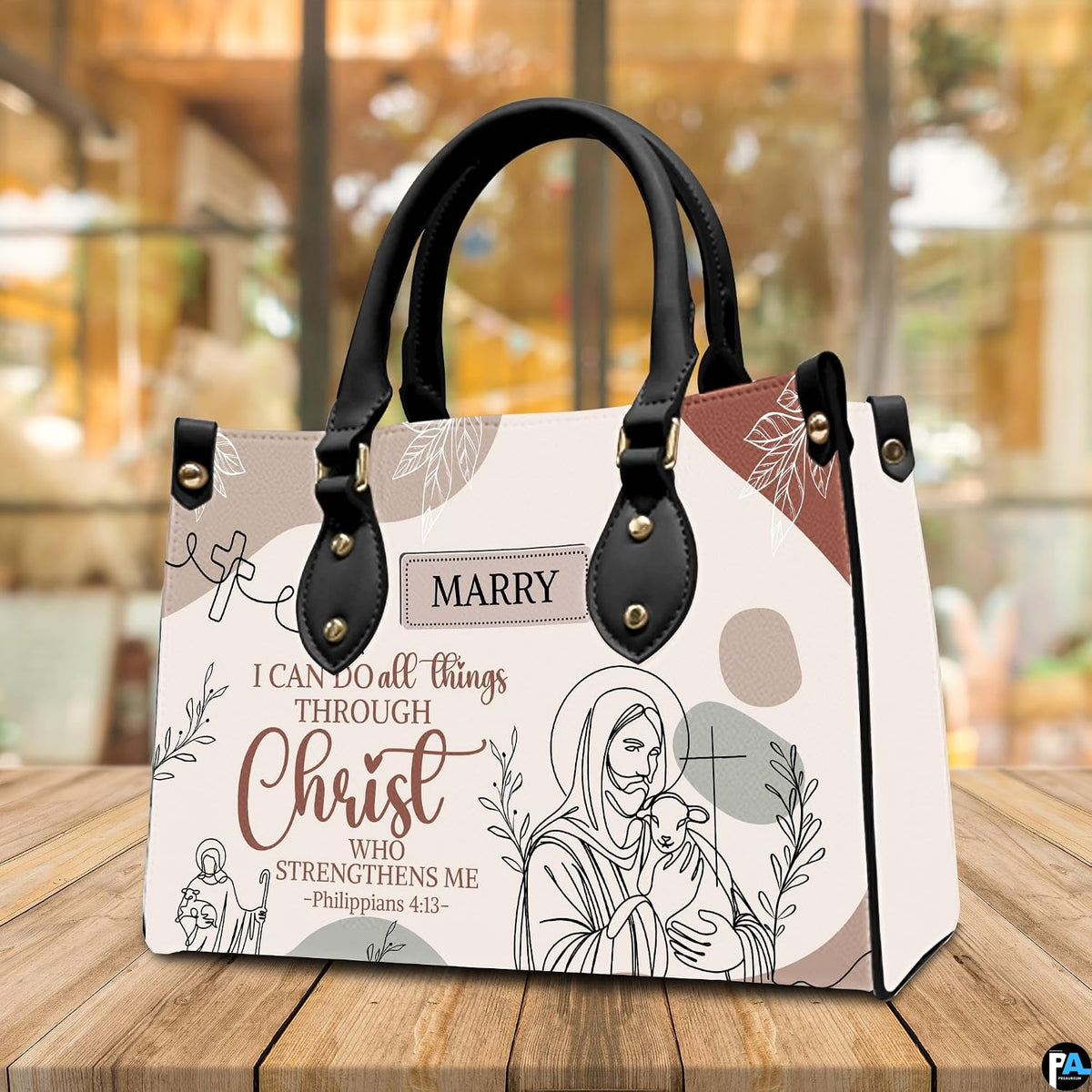 Jesus line art handbag displayed on wooden tabletop in front of sunlit cafe window.