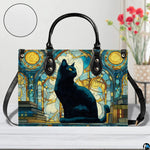 Front view of black cat on books stained glass art on white tabletop beside red blossoms.