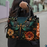 Front view of dragonfly handbag featuring emerald wings and blooming amber dahlias on dark slate teal