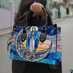 Model wearing dark coat carrying the stained glass Virgin Mary handbag over shoulder on a city walkway.