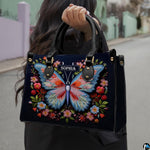 Woman carrying the navy embroidered butterfly handbag outdoors on a city sidewalk.