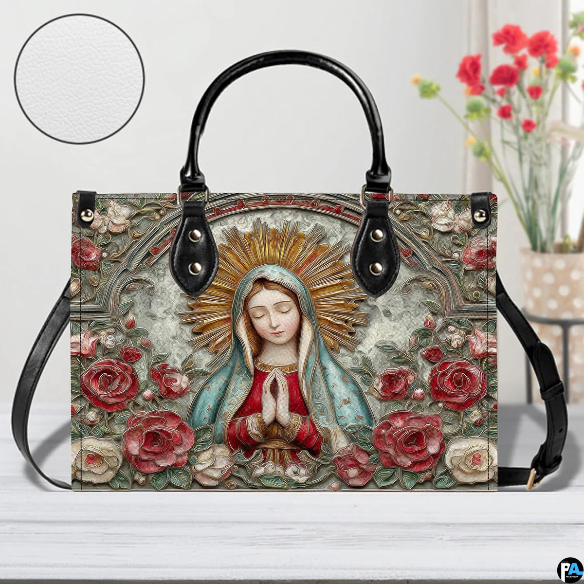 Tabletop lifestyle display of Our Lady of Guadalupe handbag beside floral bouquet.