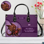 Book dragon violet handbag on white wooden table beside floral vase with detail inset.
