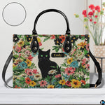 Close-up front view of green-eyed black cat and colorful garden florals on structured tote handbag