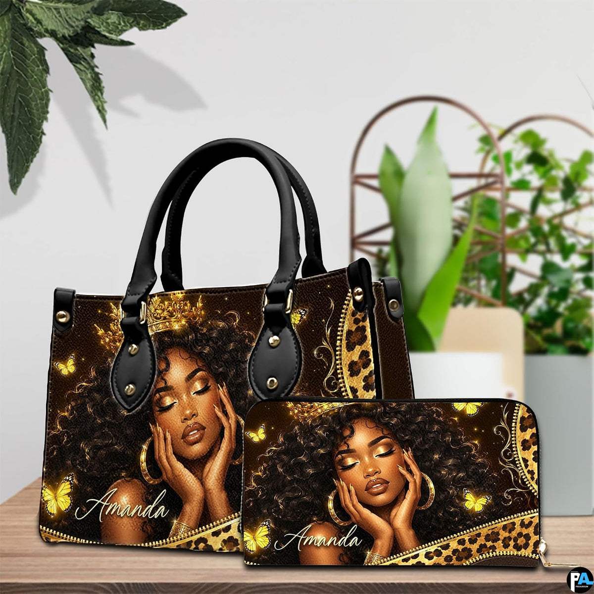 Black woman butterfly art print placed on wooden tabletop beside green houseplant leaves.