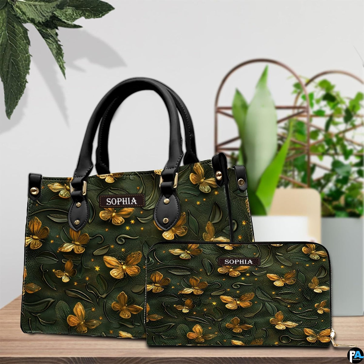 Top-handle handbag and matching wallet shown together on a tabletop beside house plants.