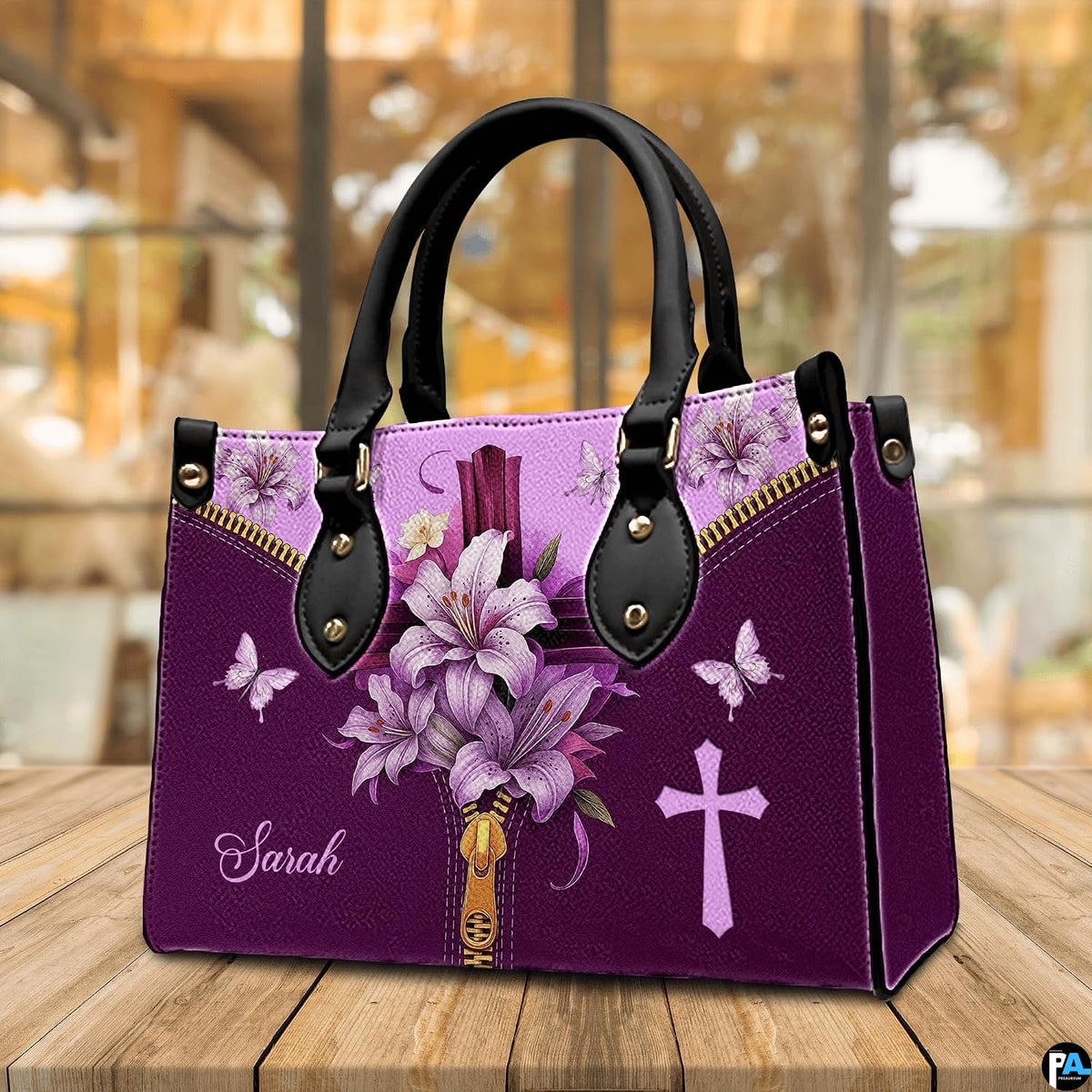 Christian cross Easter lily violet handbag displayed on wooden tabletop in front of sunlit windows.