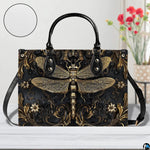 Front view of gold dragonfly handbag on white table with floral vase and texture swatch inset
