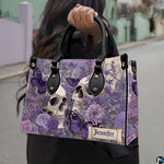 Lavender skull handbag carried outdoors by top handle on residential street.