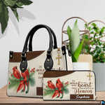 Red cardinal remembrance handbag and matching wallet displayed on a wooden surface beside green foliage.