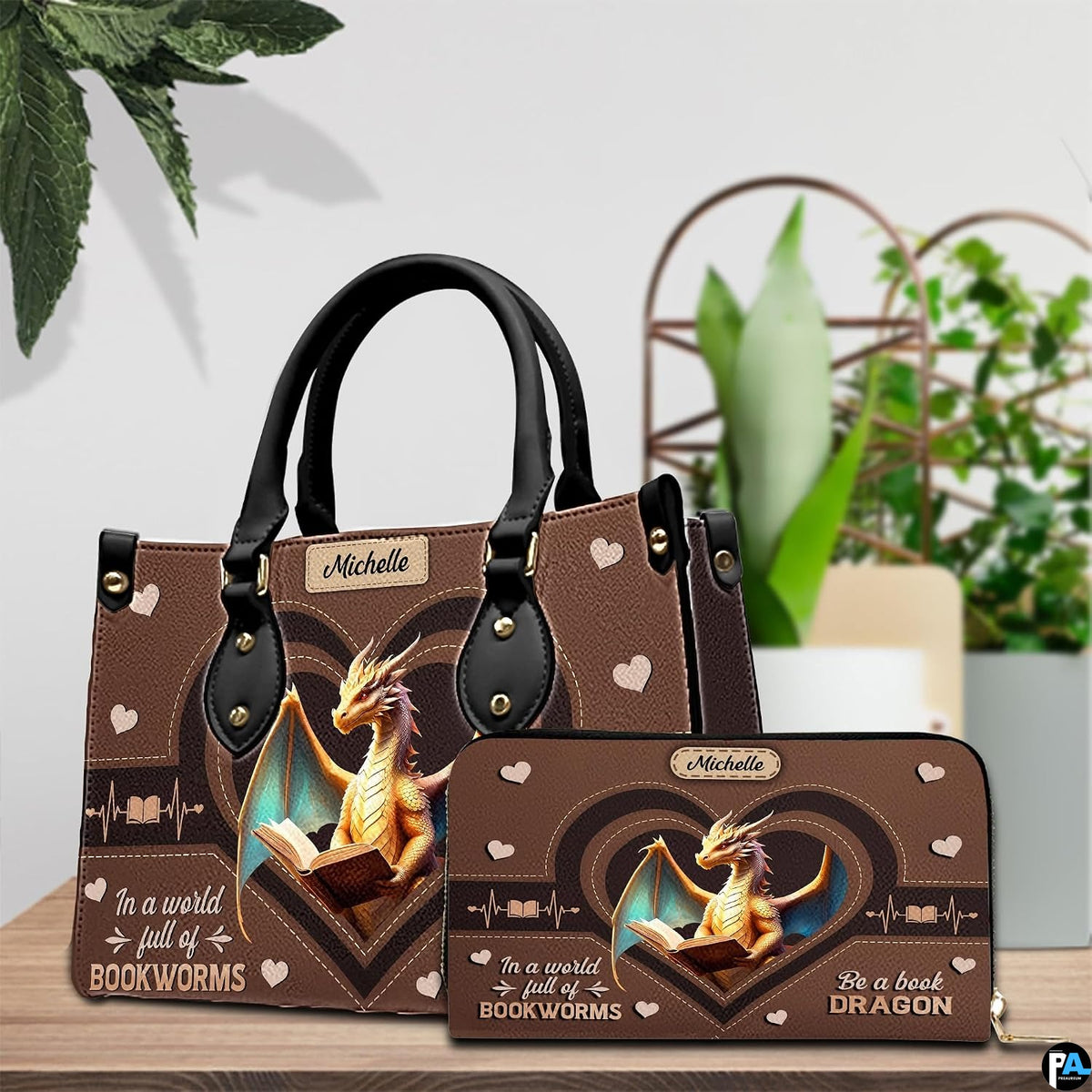 Handbag displayed alongside matching zippered wallet with heart dragon artwork on wooden table with houseplant