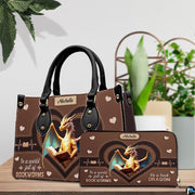 Handbag displayed alongside matching zippered wallet with heart dragon artwork on wooden table with houseplant