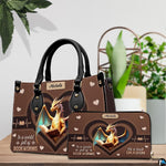Handbag displayed alongside matching zippered wallet with heart dragon artwork on wooden table with houseplant