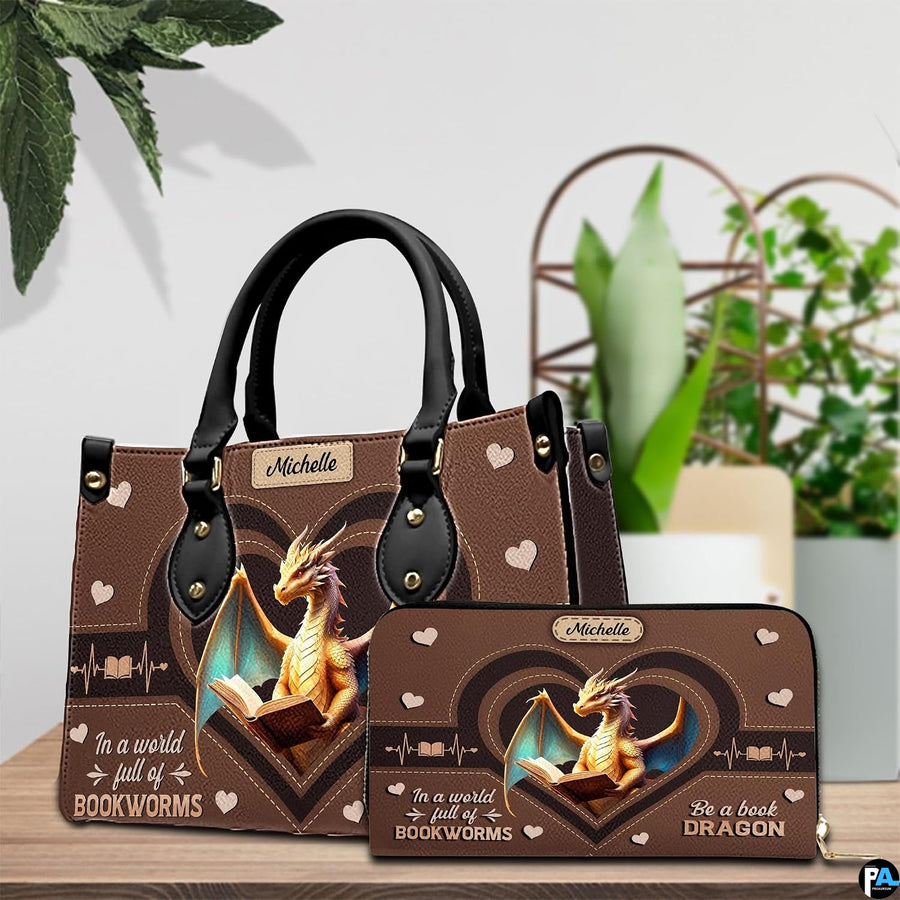 Handbag displayed alongside matching zippered wallet with heart dragon artwork on wooden table with houseplant