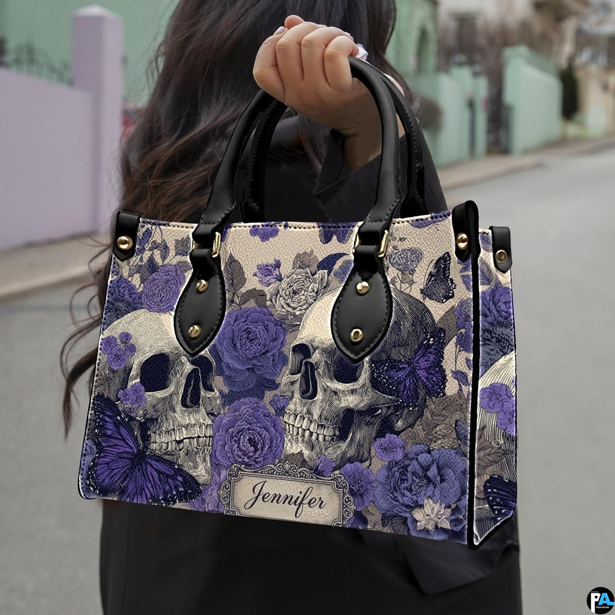 Violet skull handbag carried outdoors by top handle along residential street.