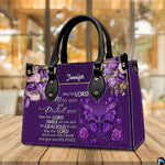 Christian blessing violet handbag displayed on wooden tabletop in front of sunlit windows.