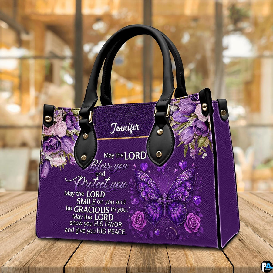 Christian blessing violet handbag displayed on wooden tabletop in front of sunlit windows.